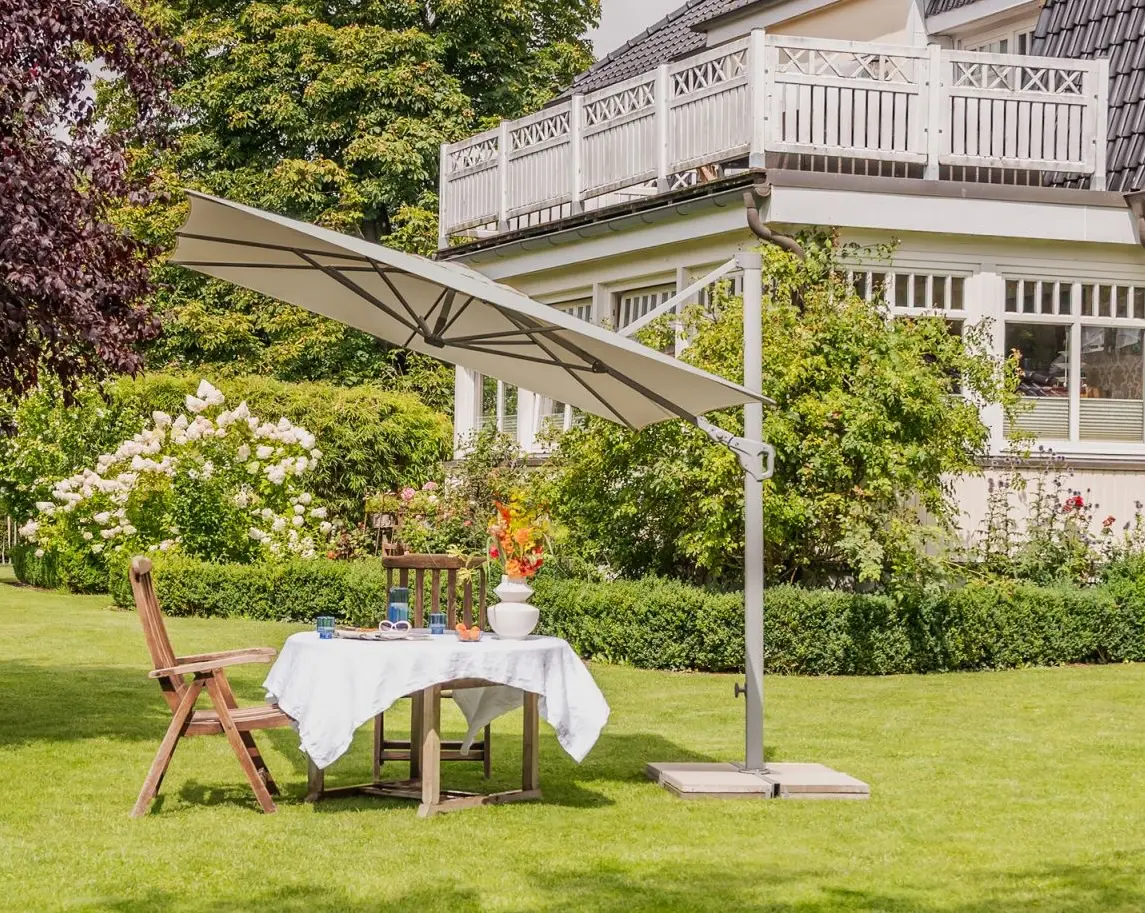 Parasol déporté inclinable Familyflex en situation sur une terrasse avec table de jardin.