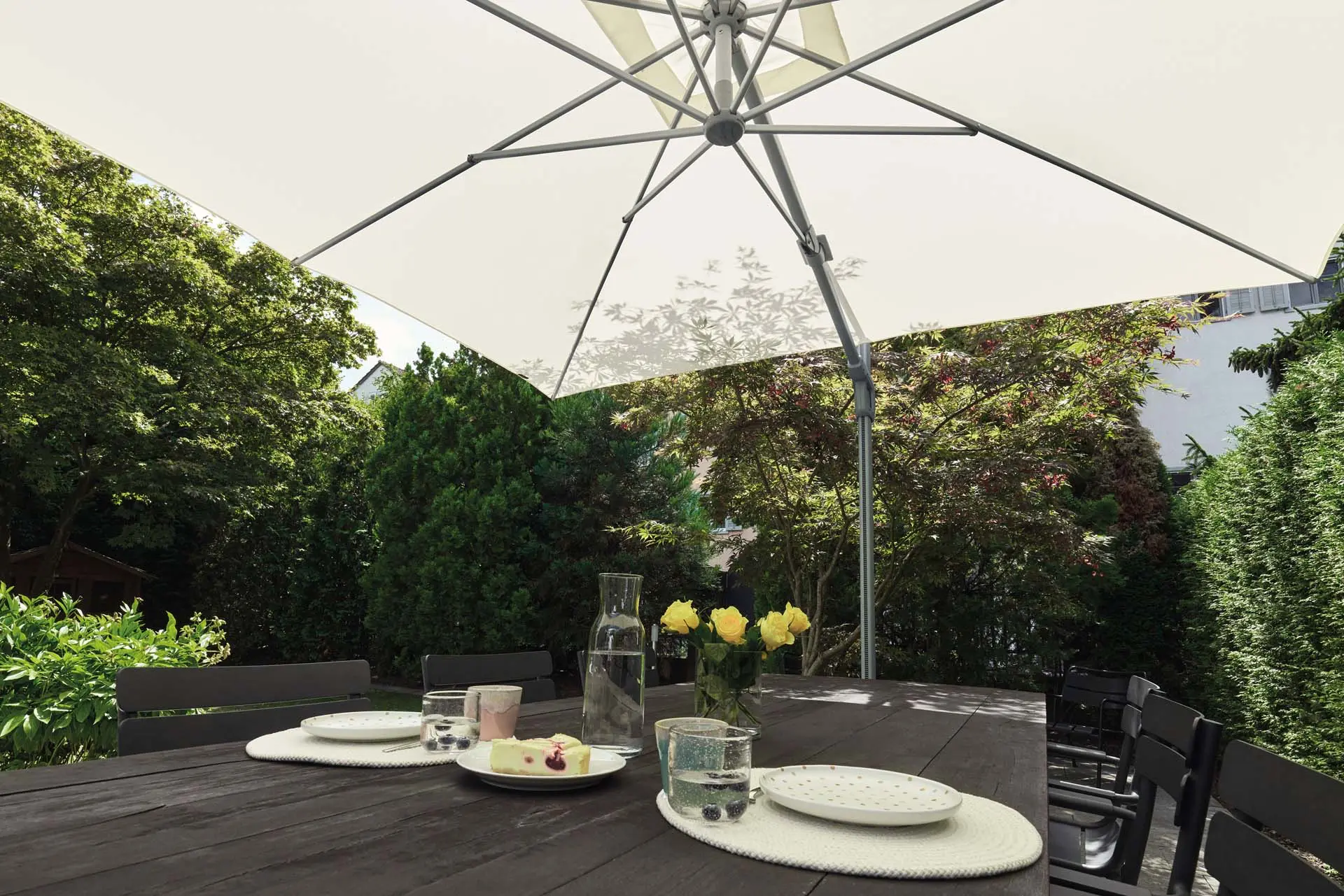 Vue de dessous du parasol déporté aluminium Sunflex protégeant une table de jardin dressée.