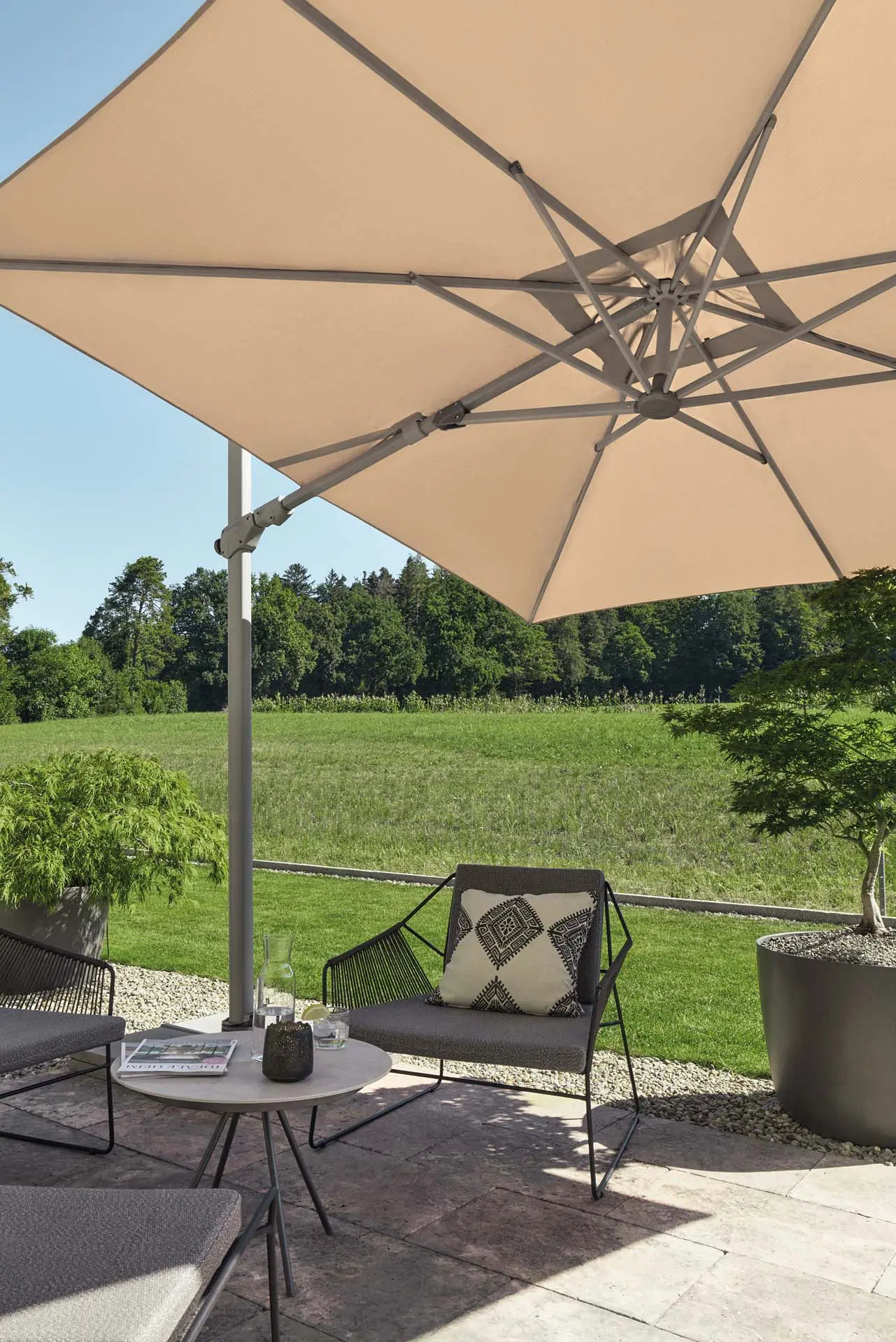Parasol déporté inclinable latéralement Varioflex coloris Light Grey 013 protégeant un salon de jardin lounge.