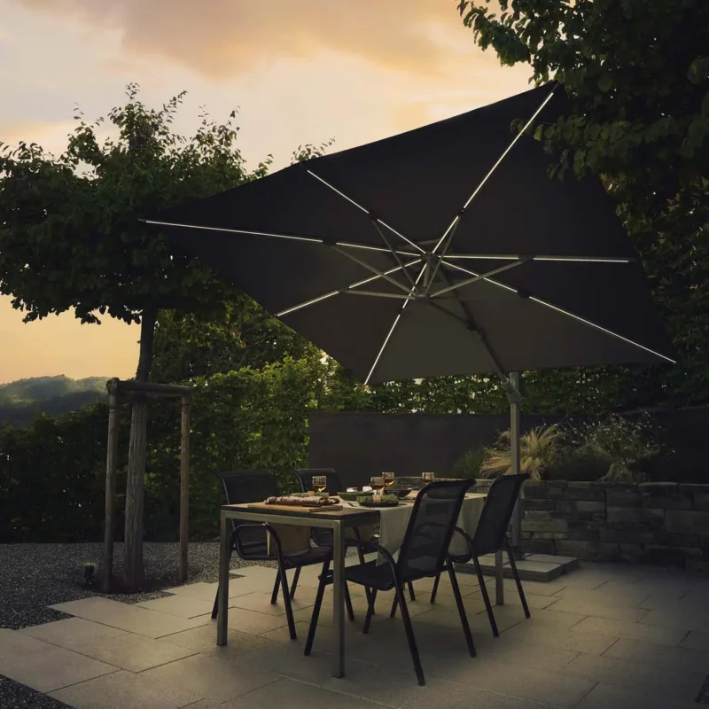 Table de jardin éclairée par un parasol déporté LED solaire Suncomfort coloris écru.