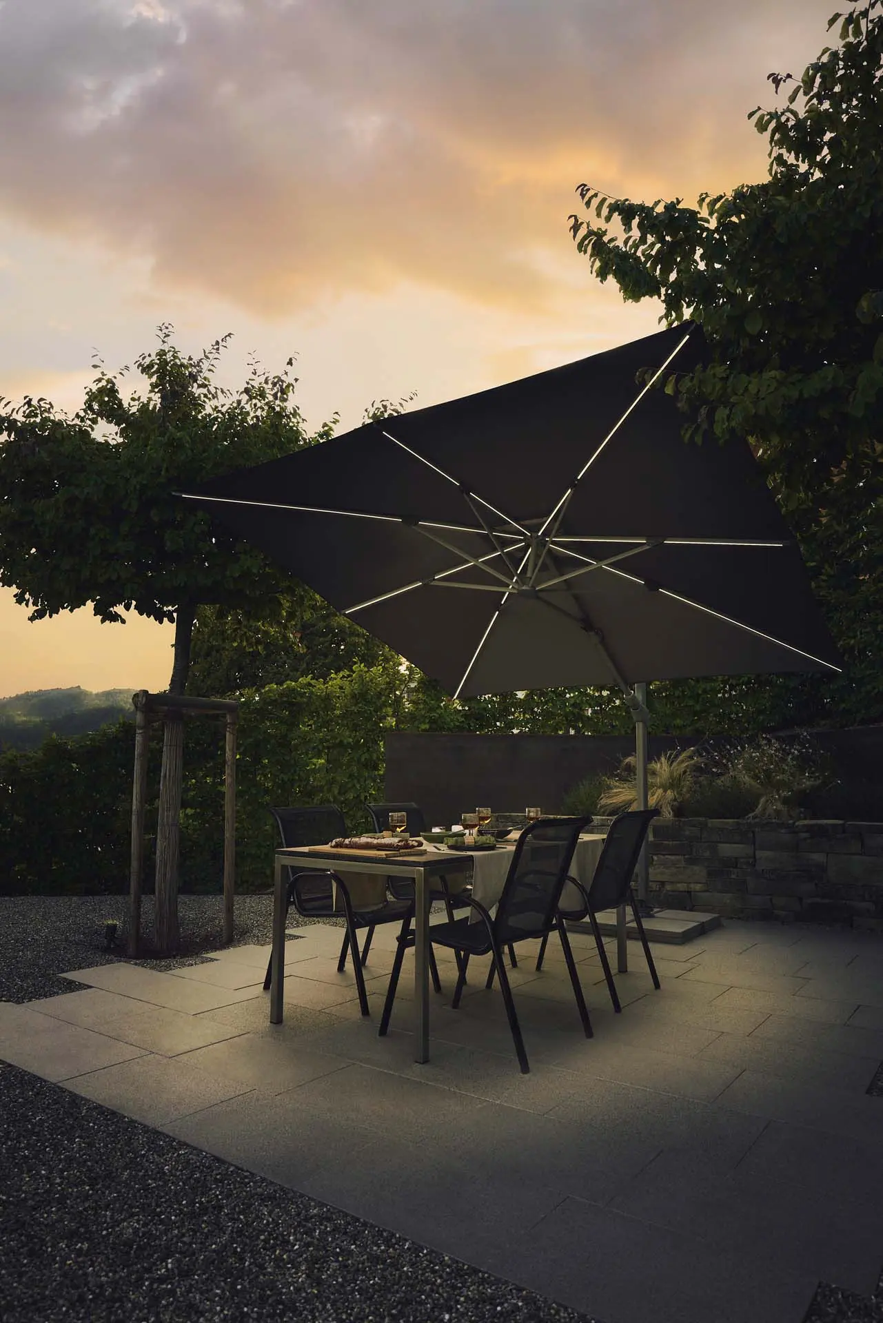 Table de jardin éclairée par un parasol déporté LED solaire Suncomfort coloris écru.