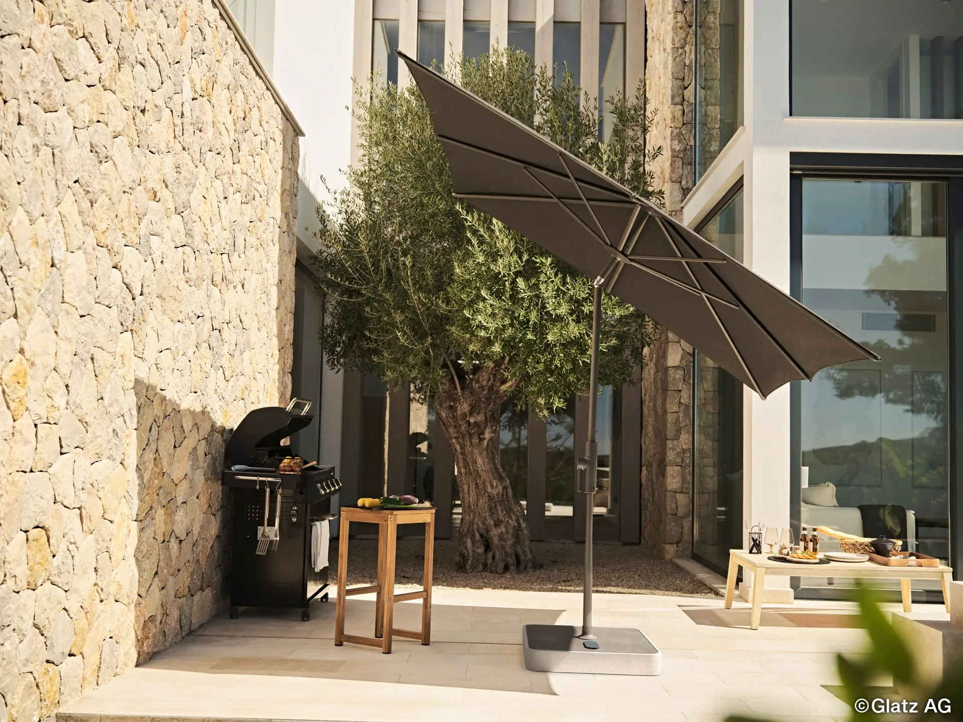 Parasol de terrasse inclinable Glatz ALU-TWIST noir à manivelle près d'un barbecue